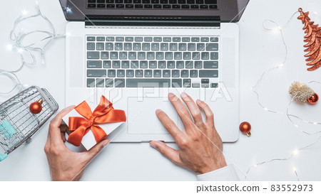 Online christmas. Gift box red ribbon, trolley and laptop, money in flat lay internet shopping composition. Winter Xmas holidays sales. 83552973