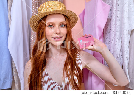 Happy Red-haired Woman At Home Shows Credit Card, Looking At Camera. 83553034