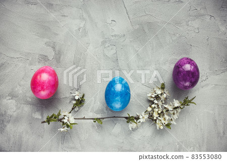 Colorful eggs and spring branch white flowers on a gray background. Easter celebration concept. Top view, flat lay, copy space Colorful eggs and spring branch white flowers on a gray background. Easter celebration concept. Top view, flat lay, copy space 83553080