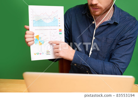 Close-up of fnancial consultant in earphones pointing at graph while explaining statistical data to client and talking to him via videoconferencing Close-up of fnancial consultant in earphones pointing at graph while explaining statistical data to client and talking to him via videoconferencing 83553194