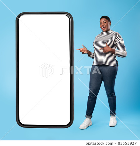 African Lady Standing Near Smartphone With Blank Screen, Blue Background African Lady Standing Near Smartphone With Blank Screen, Blue Background 83553927