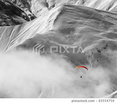 Paragliding at snow mountains in haze. Black and white toned image. Selective color effect. Paragliding at snow mountains in haze. Black and white toned image. Selective color effect. 83554759