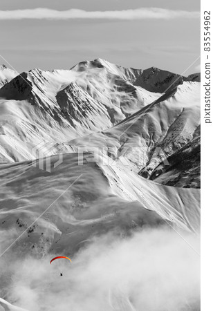Paragliding at snow mountains in haze. Black and white toned image. Selective color effect. Paragliding at snow mountains in haze. Black and white toned image. Selective color effect. 83554962