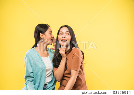 woman surprised when her friend talks whispering in her ear with copyspace 83556914