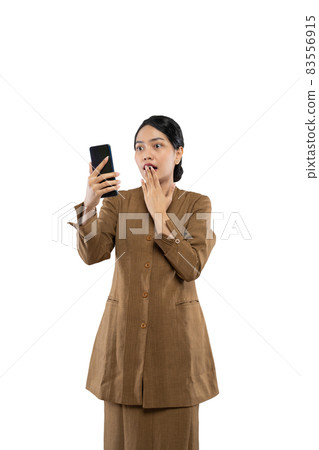Shocked woman in uniform covering mouth while looking at her phone Shocked woman in uniform covering mouth while looking at her phone 83556915