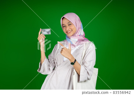 asian girl in hijab smiling while holding atm card with finger gesture pointing asian girl in hijab smiling while holding atm card with finger gesture pointing 83556942