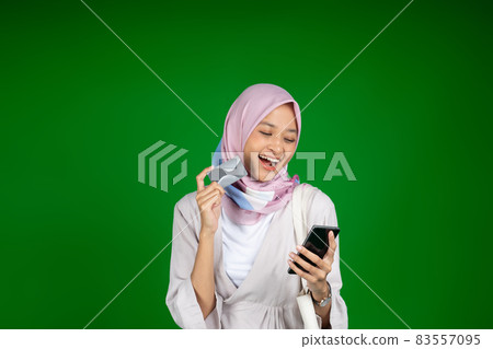 Excited woman in hijab using mobile phone while holding atm card 83557095