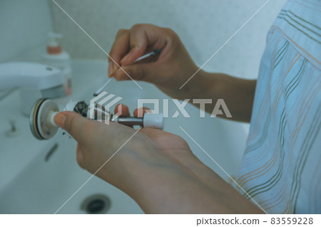 Housewife cleaning the drain of the washbasin 83559228