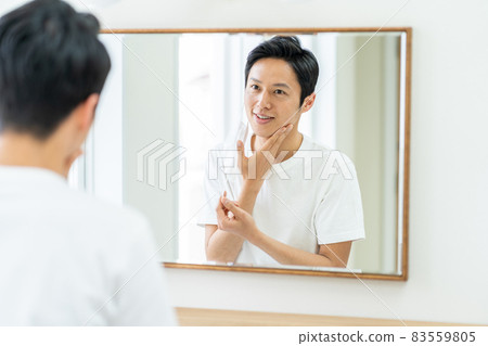 A man checking the condition of troubled skin on a mask in the bathroom. A man checking the condition of troubled skin on a mask in the bathroom. 83559805