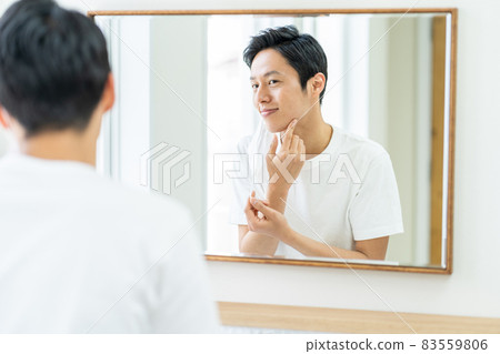 A man checking the condition of troubled skin on a mask in the bathroom. 83559806
