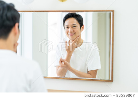 A man checking the condition of troubled skin on a mask in the bathroom. 83559807