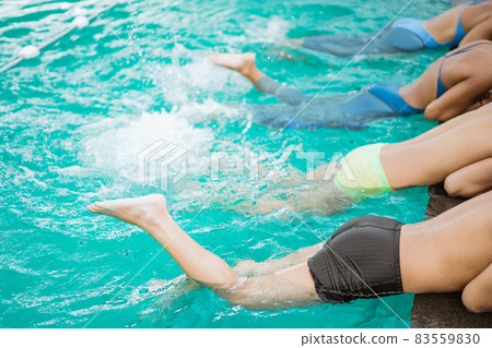 close up of four teenage legs lying by the pool with their feet making waves 83559830