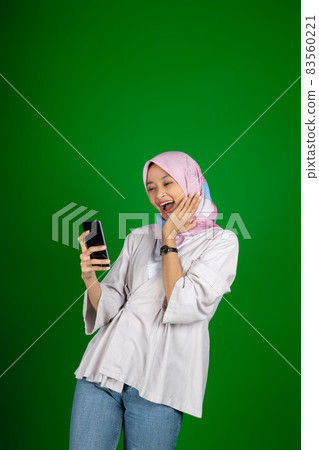 Muslim girl in headscarf laughs in surprise when looking at mobile phone screen Muslim girl in headscarf laughs in surprise when looking at mobile phone screen 83560221