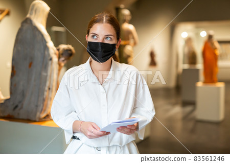 Positive female in protective mask with paper guide exploring sculpture art pieces in gallery Positive female in protective mask with paper guide exploring sculpture art pieces in gallery 83561246