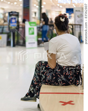 Back view of Asian woman wear face mask to prevent Corona virus (Covid-19) sit and look up phone numbers from a small notebook in public place and keep social distancing with other people. New normal. 83562807