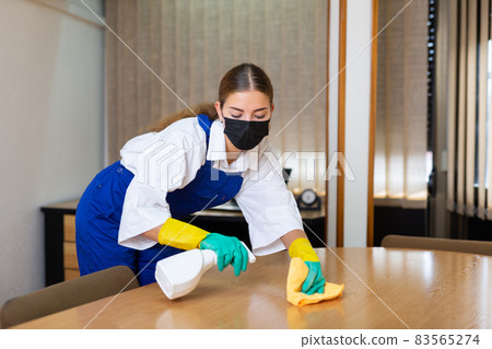 Portrait of a young woman worker in a protective mask, washing an office desk 83565274