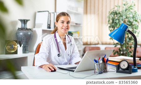 Smiling young female doctor working with laptop in office 83565360
