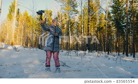 Professional Videographer Holding DSLR Camera on 3-axis Gimbal Stabilization Device in Winter. Cinematographer Operator. Slow Motion Professional Videographer Holding DSLR Camera on 3-axis Gimbal Stabilization Device in Winter. Cinematographer Operator. Slow Motion 83565554