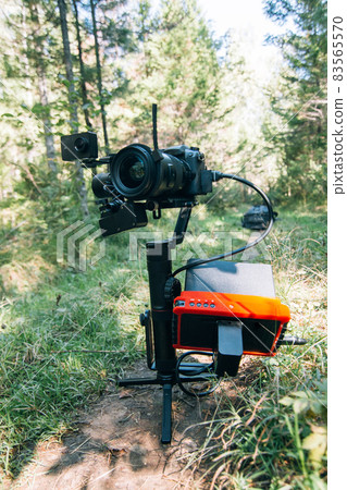 Professional DSLR Camera on 3-axis Gimbal Stabilization Device in Forest. Cinematographer Operator. Slow Motion Professional DSLR Camera on 3-axis Gimbal Stabilization Device in Forest. Cinematographer Operator. Slow Motion 83565570