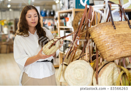Young woman choosing straw bag at store 83566263