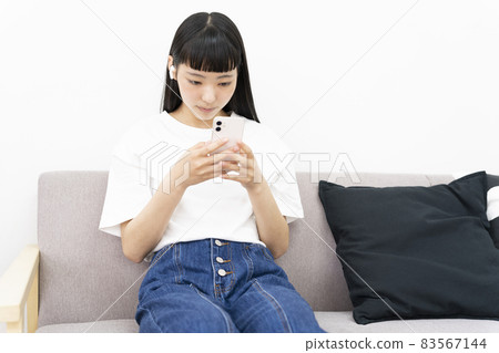 A young woman sitting on the sofa and operating her smartphone while looking down 83567144