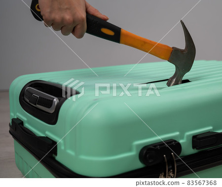 A woman hits a suitcase with a hammer on a white background. 83567368