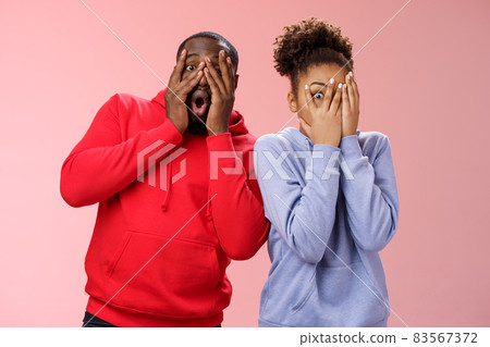 Funny cute carefree loving african american boyfriend girlfriend fool around hide faces palms peeking through fingers mimicking joking around make funny mimics, standing pink background surprised 83567372