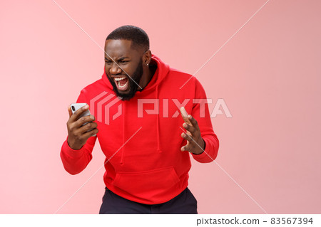 Angry furious african-american bearded guy lose control emotions shouting outraged annoyed smartphone display look phone insane stooping frowning rage, standing irritated pink background 83567394