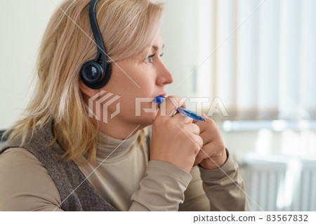 A thoughtful middle-aged blonde with a headset and a pen in her hands. copy space. A thoughtful middle-aged blonde with a headset and a pen in her hands. copy space. 83567832