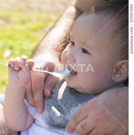 Half-baby holding a spoon on his father's lap 83567894