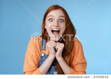 Cute redhead european girl blue eyes freckles reacting amused shocking rumor lift eyebrows drop jaw surprised smiling excited picked get role theatre play rejoicing astonished blue background 83568628