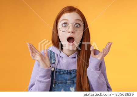 Close-up shocked sensitive concerned young panicking redhead woman worry drop jaw gasping raise hands spread freak out stare surprised emotional reacting incredible news, orange background 83568629