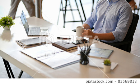 Businessman sits in his workplace, drink a morning coffee during looks on laptop screen. Businessman sits in his workplace, drink a morning coffee during looks on laptop screen. 83569818