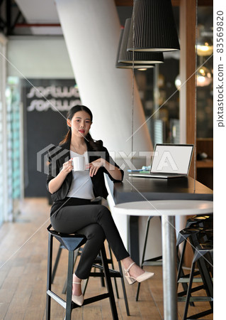 Elegant Asian young businesswoman sits on the chair and hold coffee cup in a modern office. Elegant Asian young businesswoman sits on the chair and hold coffee cup in a modern office. 83569820