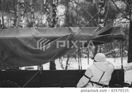 Hidden Re-enactor Dressed As German Wehrmacht Infantry Soldier In World War II Sitting In Ambush Near Peasant Cart In Winter Forest And Looking At Old Army Binoculars. Historical Re-enactment. WWII Hidden Re-enactor Dressed As German Wehrmacht Infantry Soldier In World War II Sitting In Ambush Near Peasant Cart In Winter Forest And Looking At Old Army Binoculars. Historical Re-enactment. WWII 83570535