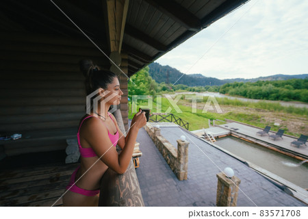 Side view portrait of a happy woman in pink swimsuit with coffee cup 83571708