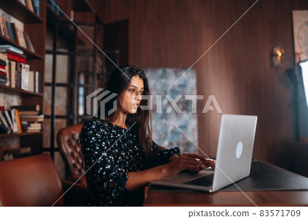 Young woman in glasses works at the laptop while sitting at table 83571709