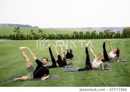 People practicing yoga on fitness mats on meadow 83571866