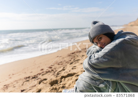 Pretty woman in warm clothes sitting on the cold autumn beach. Pretty woman in warm clothes sitting on the cold autumn beach. 83571868