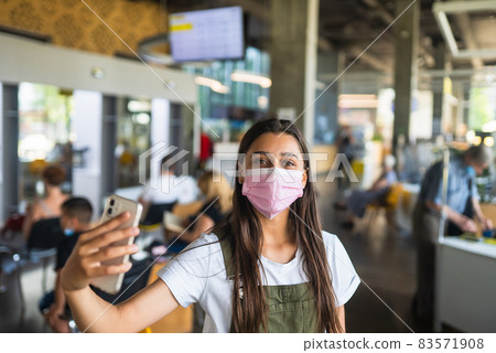Young woman in pink face mask uses smartphone at indoor. 83571908