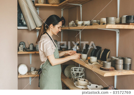 Portrait of young woman with finished production in pottery workshop. Portrait of young woman with finished production in pottery workshop. 83572769