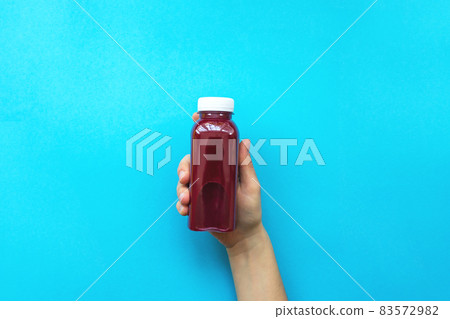 Female hands holding plastic bottles with red juice or smoothie on blue background.  83572982