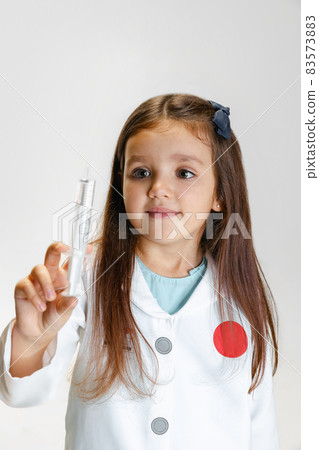 Portrait of cute beautiful girl, child in image of doctor wearing white lab coat with toy syringe isolated on white studio background 83573883
