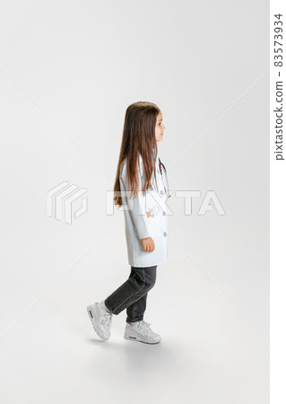 Side view. Cute beautiful little girl, child in image of doctor wearing white lab coat posing isolated on white studio background 83573934