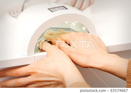 Female hand with manicured fingers dry inside UV light machine in manicure salon. Female hand with manicured fingers dry inside UV light machine in manicure salon. 83574667