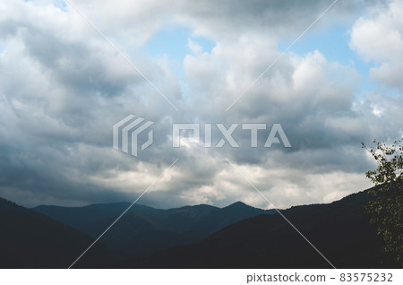 Thick white clouds over mountains covered with green forest Thick white clouds over mountains covered with green forest 83575232