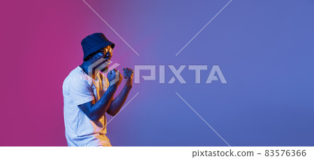 Winning success happy man celebrating being a winner. Dynamic image of male model on gradient purple pink studio background in neon Winning success happy man celebrating being a winner. Dynamic image of male model on gradient purple pink studio background in neon 83576366