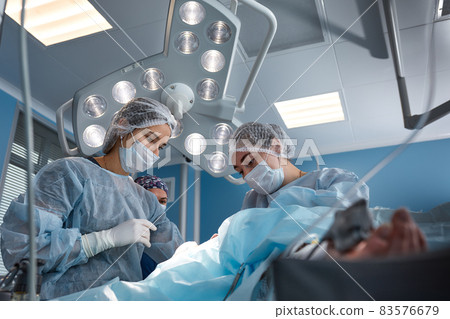 Concentrated Surgical team operating a patient in an operation theater. Well-trained anesthesiologist with years of training with complex machines follows the patient throughout the surgery Concentrated Surgical team operating a patient in an operation theater. Well-trained anesthesiologist with years of training with complex machines follows the patient throughout the surgery 83576679
