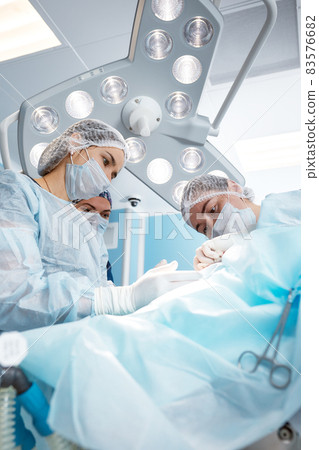 Concentrated Surgical team operating a patient in an operation theater. Well-trained anesthesiologist with years of training with complex machines follows the patient throughout the surgery 83576682