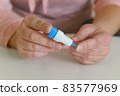 The woman uses a lancing device to take a blood sample from her finger 83577969
